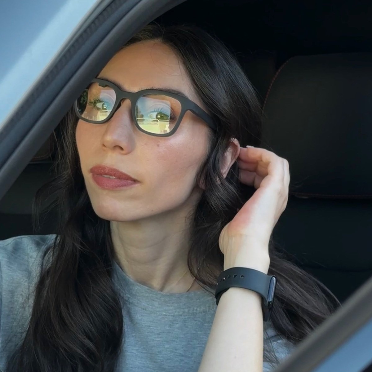 A wearer in a car wearing Halo, the matte black frame reading as ordinary glasses, one hand raised to the temple